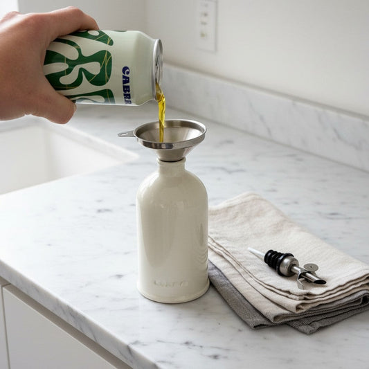 Cabra Olive Oil refill set with a ceramic bottle, stainless steel funnel, and pourer on a marble countertop.